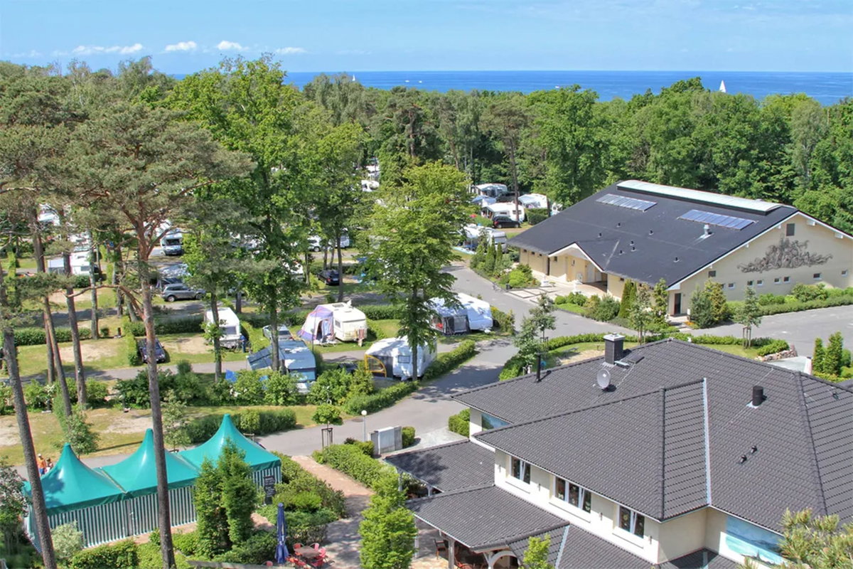 Camping.info n. 1 in Germania: il campeggio Kühlungsborn. Puoi vedere una vista aerea di un campeggio in campagna, con il mare sullo sfondo.